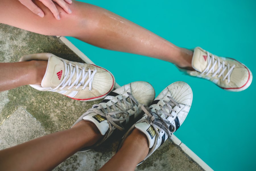 Beine Jugendlicher am Poolrand mit Sneaker