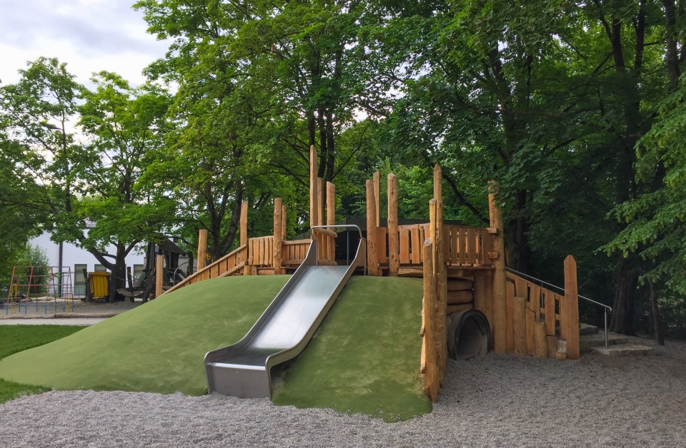 Rutsche auf einem Grashügel mit Holzklettergerüst im Kindergarten St. Hildegard