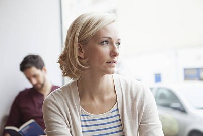 Frau schaut traurig, während Mann im Hintergrund liest