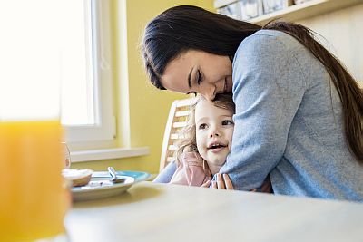 Mutter und Tochter am Küchentisch, Mutter drückt Kind liebevoll an sich