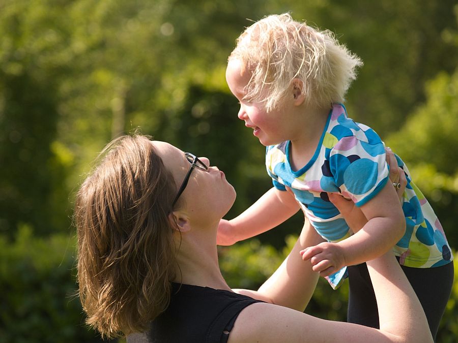 Mutter hält ihr Kind mit beiden Armen über sich, das Kind freut sich