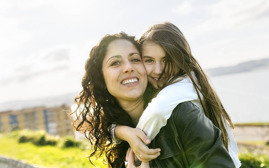 Teenager-Tochter umarmt seine Mutter lachend