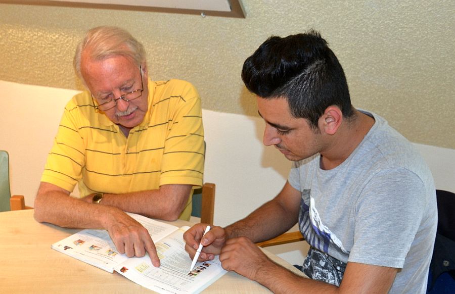 Älterer Mann gibt jungem Flüchtling Unterricht, sie schauen gemeinsam in ein Buch.