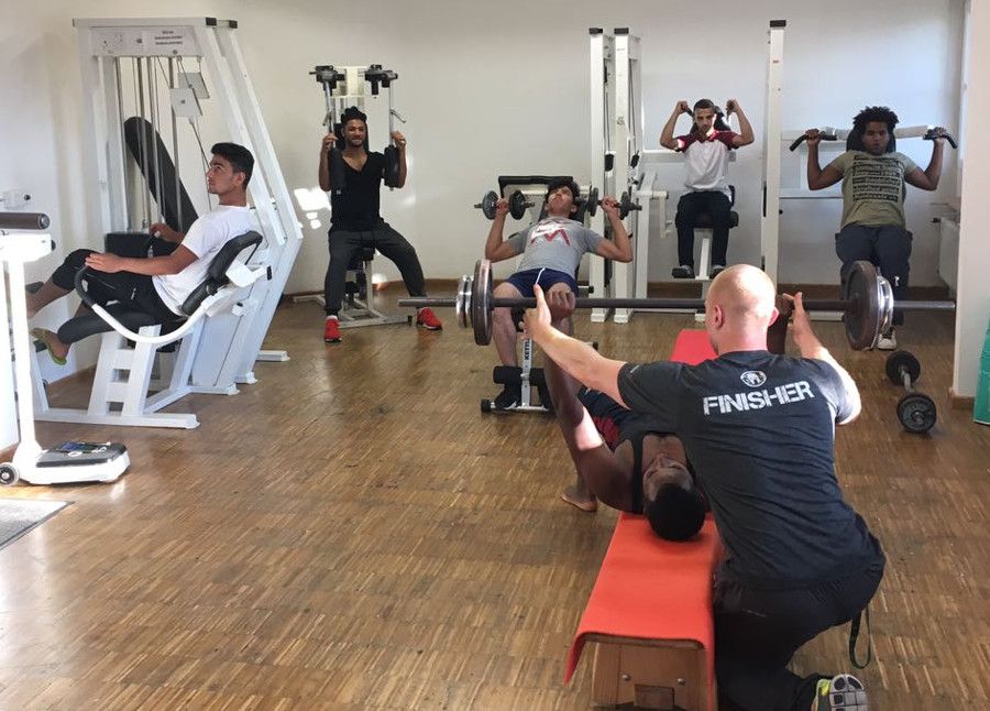 Trainer leitet junge Männer bei der Nutzung von Fitnessgeräten an.