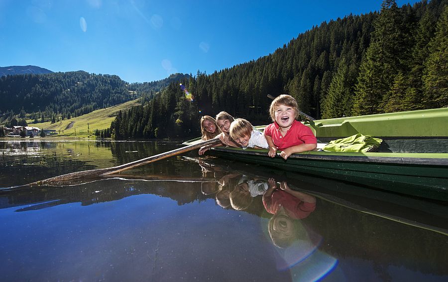Kinder liegen entspannt in einem Ruderboot, das auf einem Bergsee treibt
