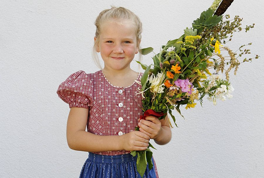 Mädchen im Dirndl hält einen  Kräuterbuschen im Arm.