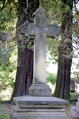 Steinernes Kreuz vor Bäumen auf einem Friedhof.