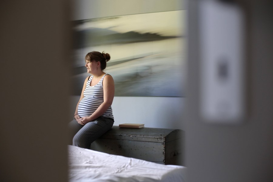 Junge schwangere Frau sitzt in Gedanken im Schlafzimmer