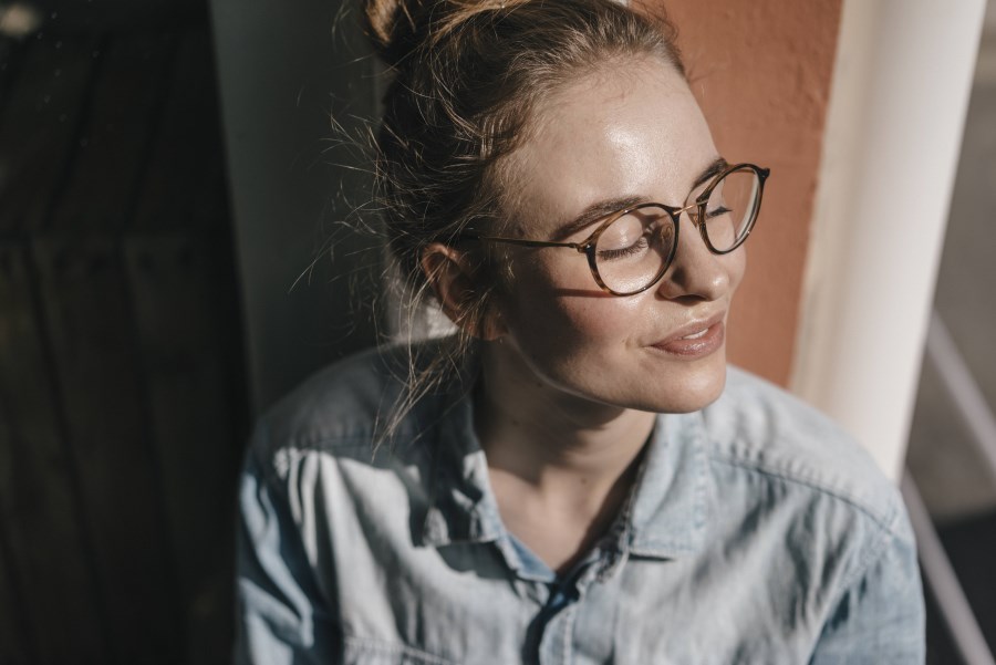 junge Frau mit Brille genießt Sonnenschein durchs Fenster