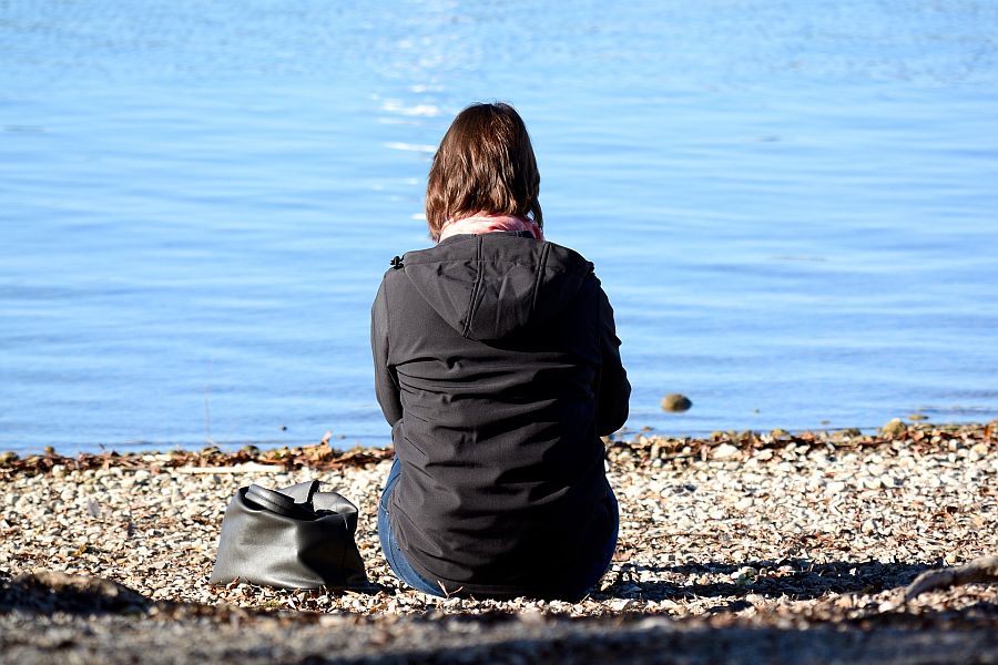 Frau in Jacke und Mütze sind mit dem Rücken zum Betrachter am See