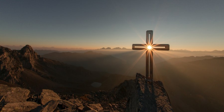 gipfelkreuz bei sonnenaufgang sonne scheint durch kreuzmitte