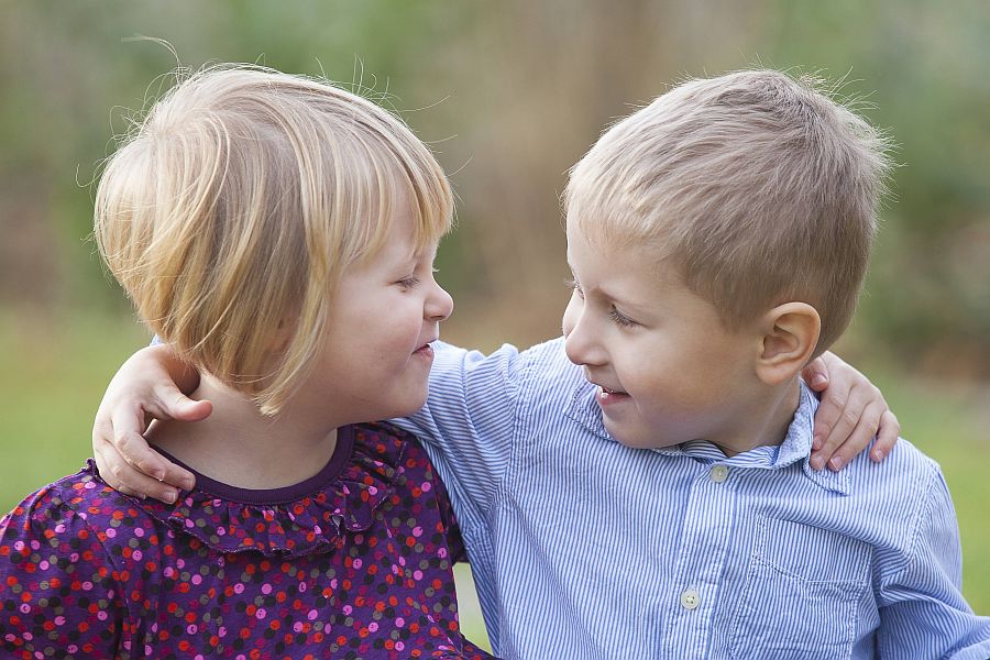 zwei kleine Kinder haben sich die Arme um die Schultern gelegt und lachen sich an