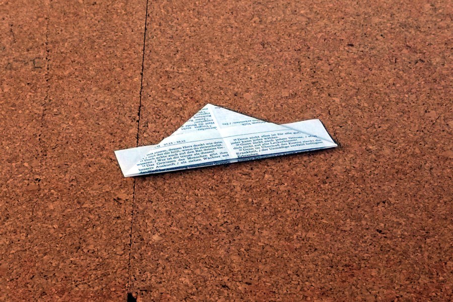 kleiner gefalteter Papierhut liegend auf Korkplatte