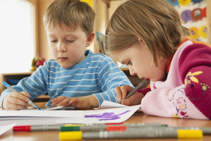junge und mädchen malen bzw. schreiben an einem Tisch im kindergarten