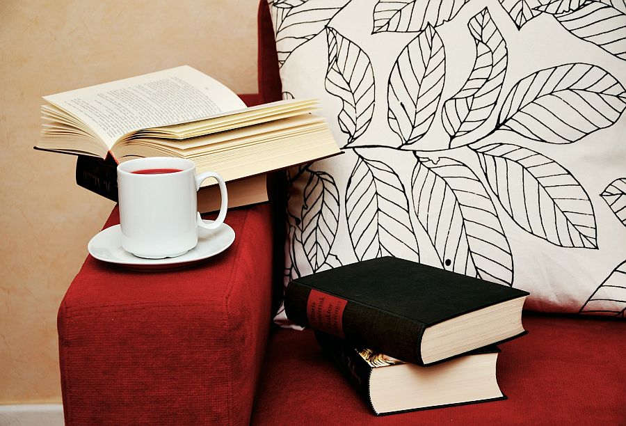 Bücher und eine Tasse Tee auf rotem Sofa