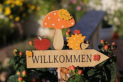 Herbstlich verziertes Holzschild im Garten mit der Aufschrift Willkommen