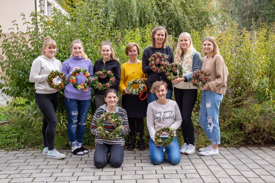 schülerinnen und lehrerin mit gebundenen herbstkränzen