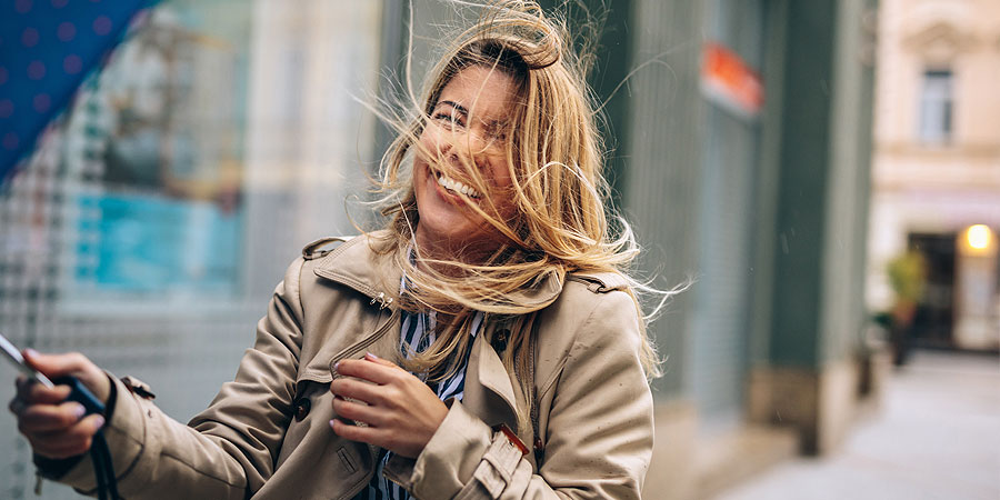 Frau im Wind mit zerzausten Haaren und Regenschirm, aber fröhlich