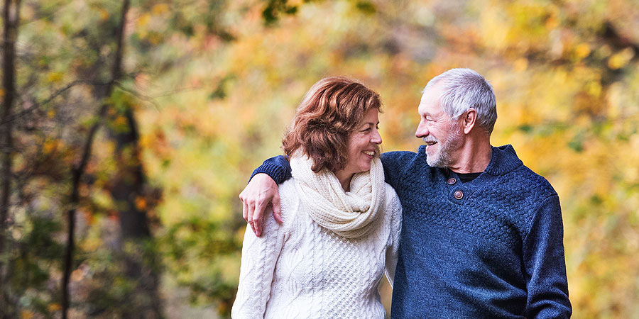 Mann und Frau gehen Arm in Arm in Herbstlandschaft spazieren