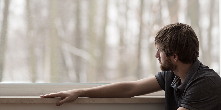 mann blickt nachdenklich aus fenster in herbstwald