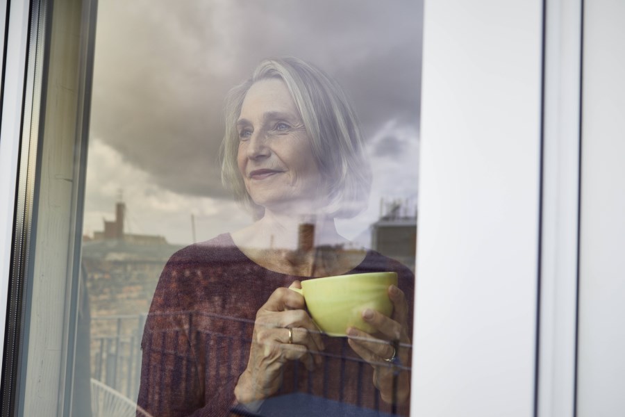 erwachsene frau blickt aus fenster mit teetasse