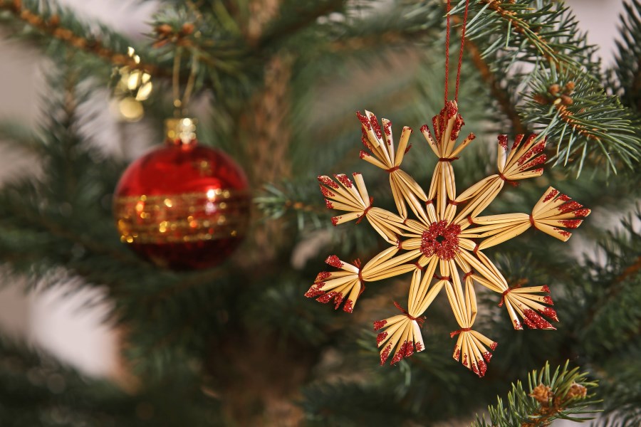 Strohstern und rote Christbaumkugel an Baum