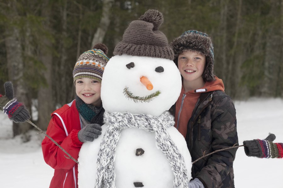 zwei Kinder stehen lächelnd hinter einem Schneemann