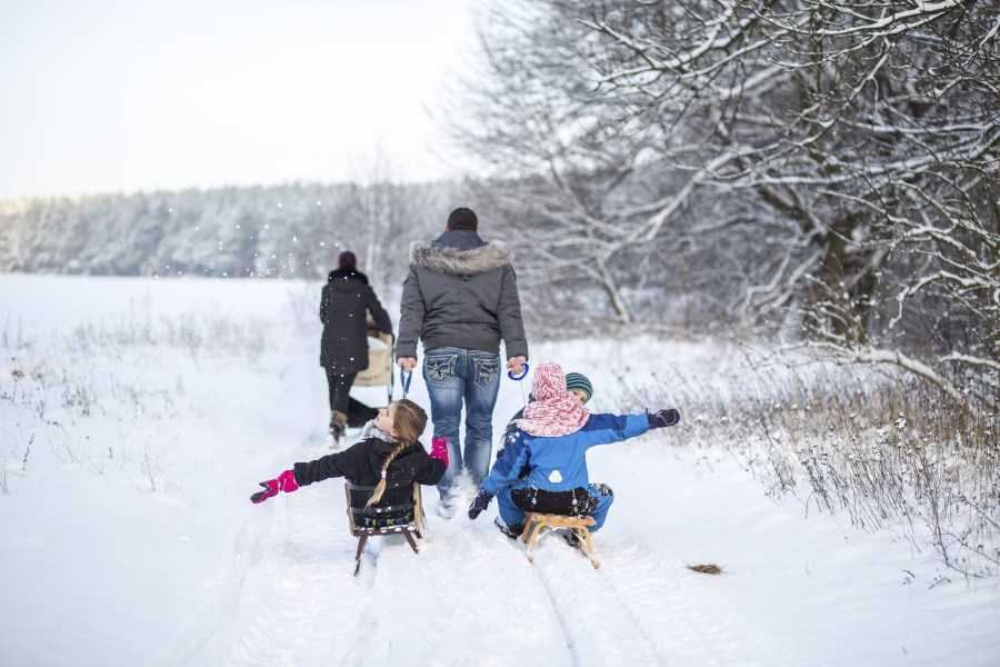 Familie macht im Schnee Spaziergang, Vater zieht zwei Kinder auf Schlitten