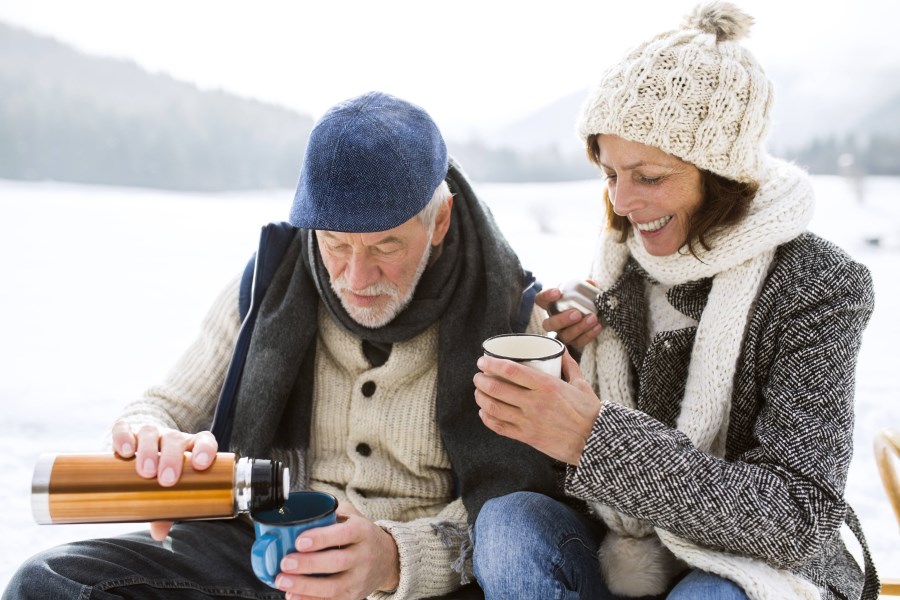 Seniorenpaar trinkt in Schneelandschaft Tee aus Thermoskanne