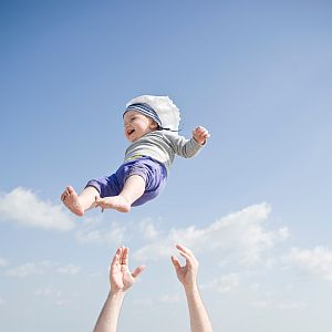 Lachendes Baby fliegt in der Luft, unter ihm zwei Hände