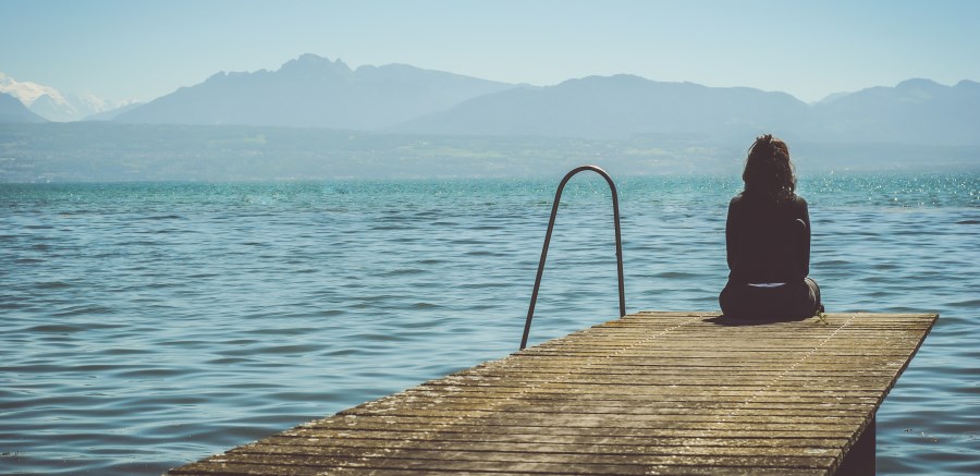 Frau sitzt an Steg am See