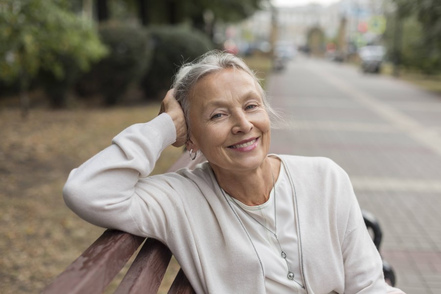 gut aussehende ältere Frau sitzt lächelnd auf einer Bank