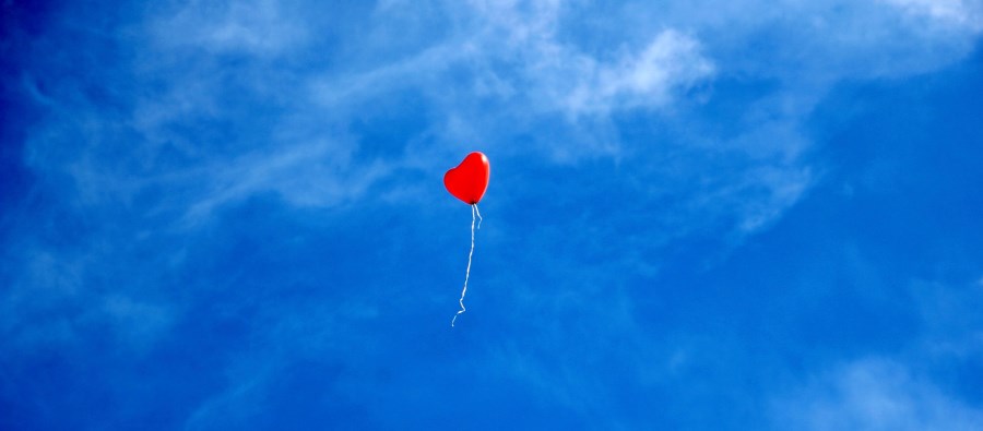 roter Herzballon fliegt in blauen Himmel_schmal