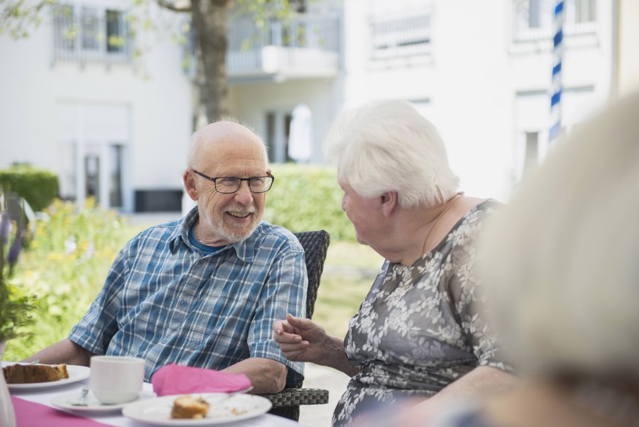 älterer Herr und ältere Dame unterhalten sich am Kaffeetisch im Garten