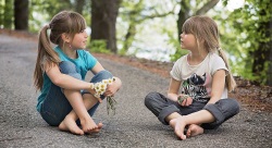 Zwei Mädchen, eins mit einem Strauß Gänseblümchen in der Hand, sitzen auf einem Weg und unterhalten sich