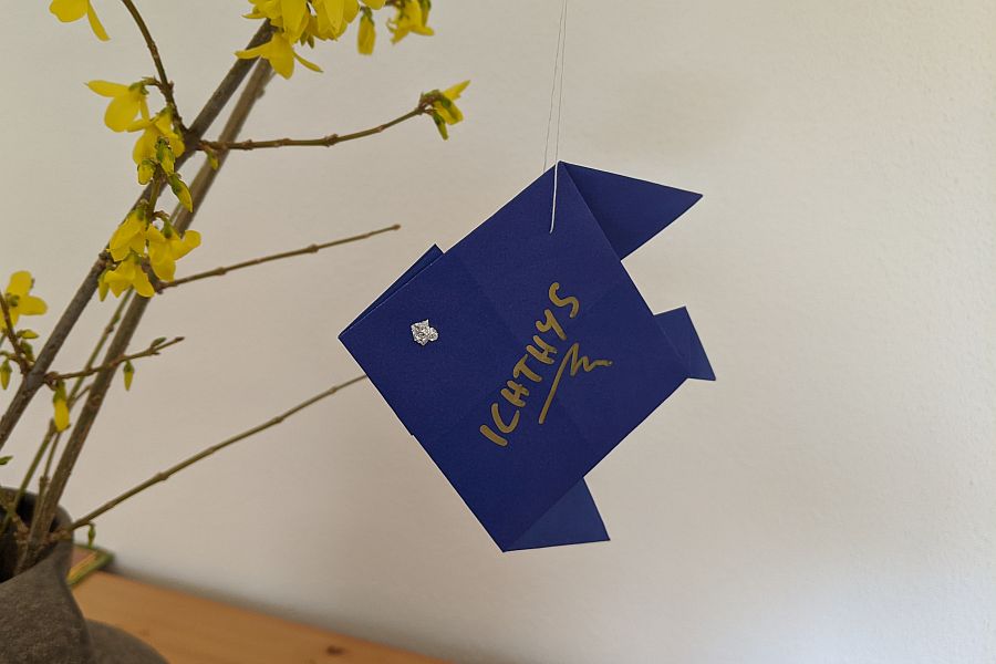 Origami-Fisch aus blauem Papier an Forsythienzweig