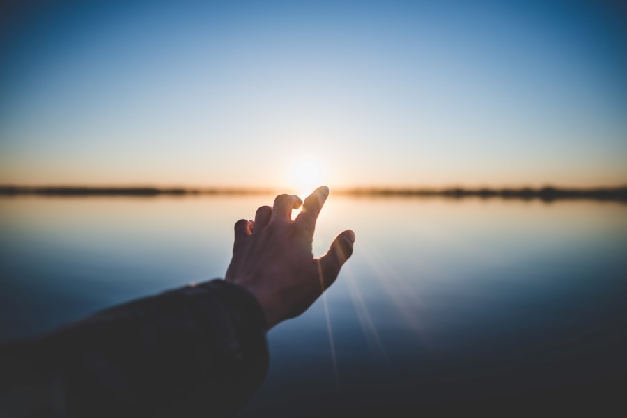 Hand streckt sich sehnsuchtsvoll in Richtung Sonnenuntergang