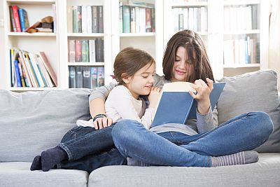 Zwei Mädchen sitzen mit Buch auf Couch