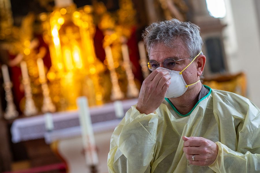 Mann in Schutzanzug hält Maske vor Nase