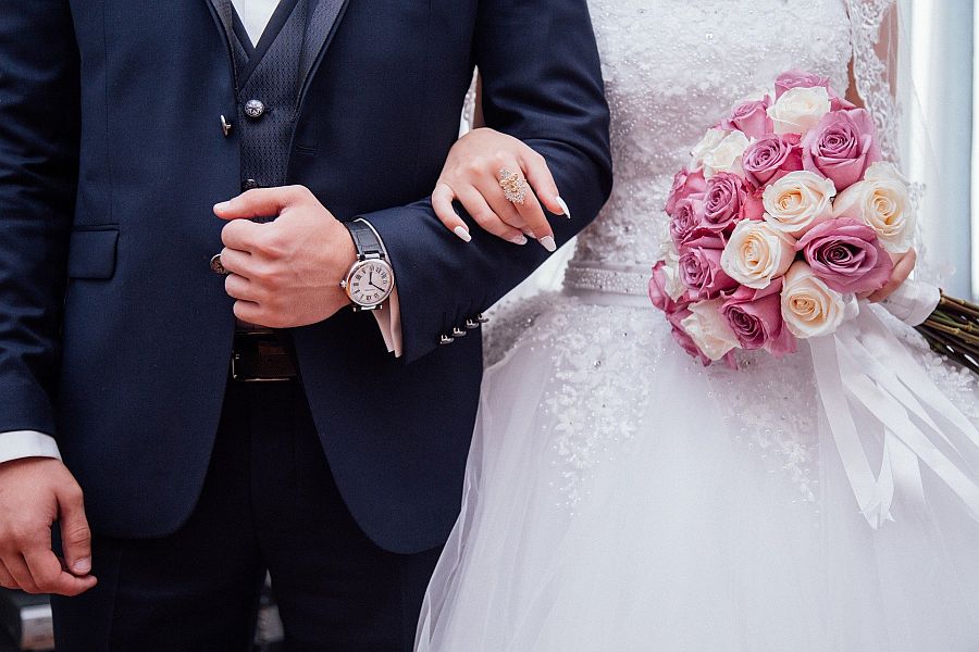 Hände von Hochzeitspaar in Hochzeitskleidung mit Brautstrauß