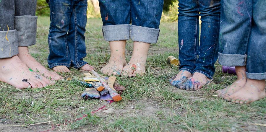fünf Paar nackte, mit Farben beschmierte Füße in Jeans