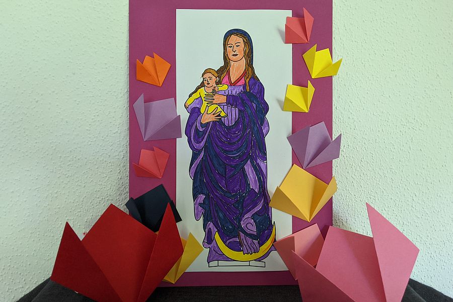 bunte Papierblumen rund um ein bunt ausgemaltes Papierbild von Maria mit Kind