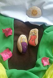 zwei mit Frauenfiguren bemalte Steine auf braunem und grünem Tuch
