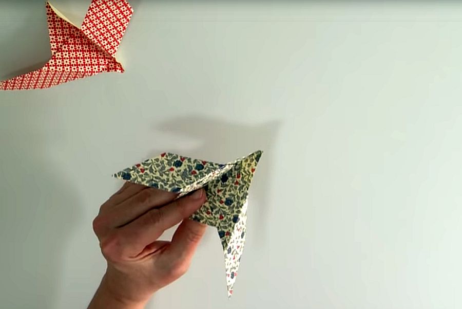 Hand hält Origami-Taube aus gemustertetem Papier, daneben zweite Taube