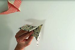 Hand hält Origami-Taube aus gemustertetem Papier, daneben zweite Taube