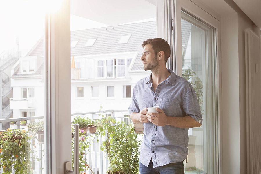 Mann mit Tasse in der Hand blickt nachdenklich aus dem Fenster