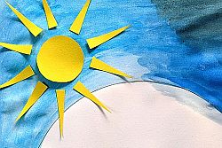 Sonne aus gelbem Tonpapier auf mit blauen Wasserfarben bemaltem Papier