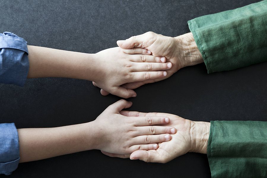 ein Paar Kinderhände und ein Paar Seniorenhände liegen ineinander