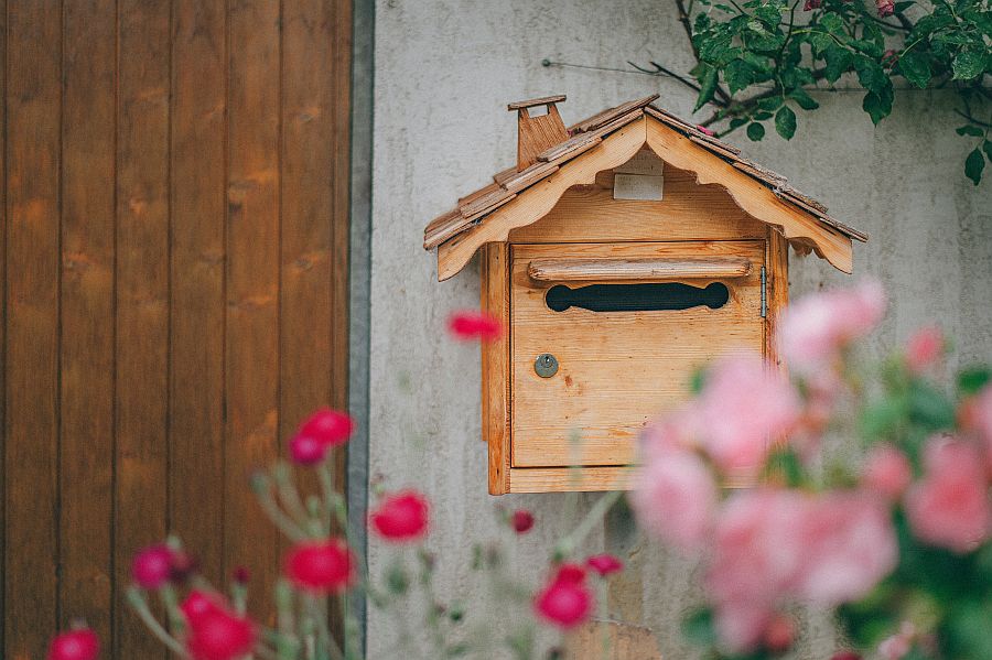 Hölzerner Briefkasten vor Haus mit Blumen