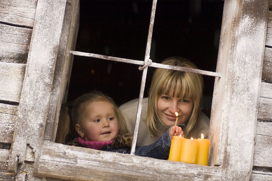 Mutter und Tochter zünden Kerzen an Fenster an